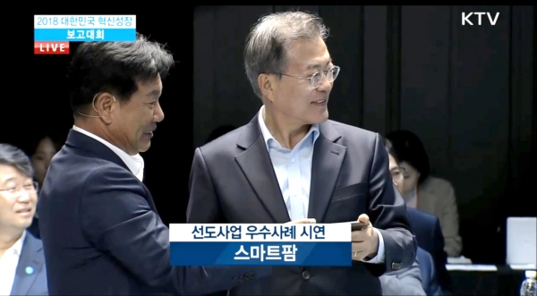 2018 대한민국 혁신성장 보고대회에서 우듬지팜김호연 대표가 ‘우듬지에 피는 혁신농업의 꿈’이라는 주제로 발표하면서 문재인 대통령과 함께 스마트폰으로 스마트팜을 원격 시연하고 있다.(사진: KTV화면 캡쳐) 2018 대한민국 혁신성장 보고대회에서 우듬지팜김호연 대표가 ‘우듬지에 피는 혁신농업의 꿈’이라는 주제로 발표하면서 문재인 대통령과 함께 스마트폰으로 스마트팜을 원격 시연하고 있다.